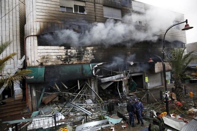 Palestinian policemen stand guard in front of a building housing Palestinian shops after a fire which was sparked by Israeli troops, in the West Bank