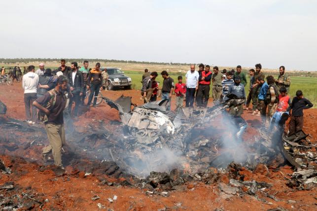 Rebel fighters and civilians gather around the wreckage of a Syrian warplane that was shot down in the Talat al-Iss area, south of Aleppo