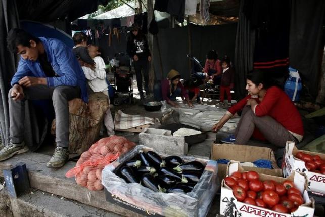 A refugee sits by his grocery stall as women cook traditional Arabic bread at a camp for refugees and migrants at the Greek-Macedonian border near the village of Idomeni