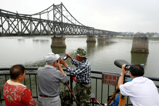 FILE PHOTO: People look through binoculars towards North Korea from the destroyed bridge across Yalu River that once linked North Korea's Sinuiju and Dandong, China's Liaoning province