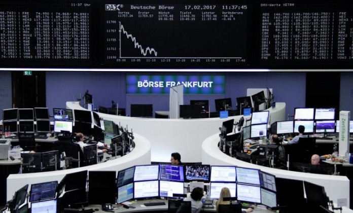 Traders work at their desks in front of the German share price index, DAX board, at the stock exchange in Frankfurt