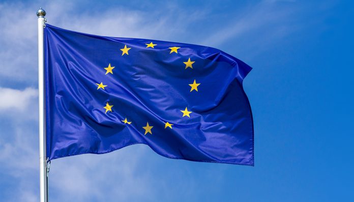 Flag of the European Union waving in the wind on flagpole against the sky with clouds, banner European Union