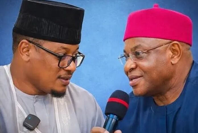 David Mark and Nafiu Bala Two men in traditional Nigerian attire converse during an interview, one holding a microphone on a blue background in a close-up shot.