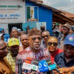 Gov Abiodun Participates In APC Primaries, Commends Peaceful Conduct Crowd of people at a political event outside a blue building with an APC sign; multiple microphones are in the foreground for press coverage.