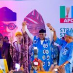 2027 Senate Race: Ogun East APC Formally Presents Dapo Abiodun As Consensus Candidate Group of Nigerian politicians on a stage at an APC event, hands raised in celebration, audience taking photos in front of a banner with the APC logo.