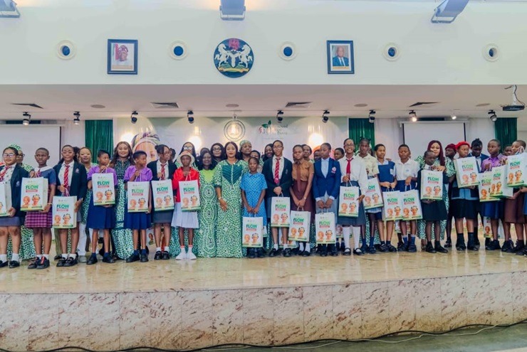 Flow with Confidence” of the Renewed Hope initiative at the Banquet Hall - THEWILL NEWS MEDIA Group of students and a few adults posing on a stage indoors, each student holding a poster or brochure.