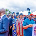 Massive Turnout As Akpabio, Bassey, Others Emerge Unopposed In APC Senate Primary In Akwa Ibom Crowd at an outdoor political rally; a man in blue attire holds a campaign poster with a portrait of a candidate.