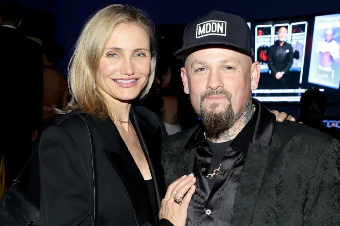 Smiling woman with blond hair and a bearded man in black attire pose together at a party or event.