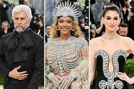 Three celebrities on a red carpet: left man in a black cape, center woman in a metallic jeweled dress with a headdress, right woman in an ornate black-and-white gown.