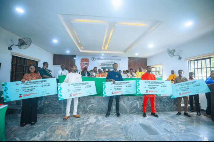 a cross-section of beneficiaries of the Hon. Ime Okon's academic grant Group of people on a stage holding oversized ceremonial checks for educational grants during a formal event inside a hall.