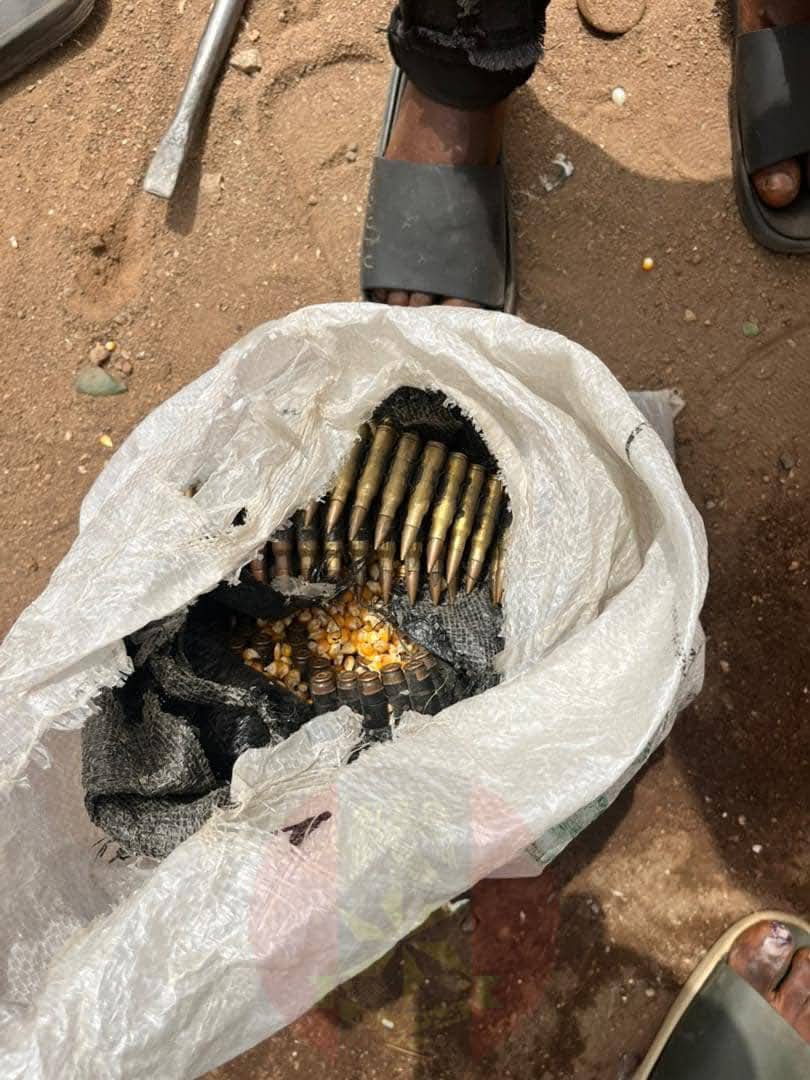 Open white plastic bag on dirt ground filled with spent ammunition rounds; toes and sandals visible at the top.