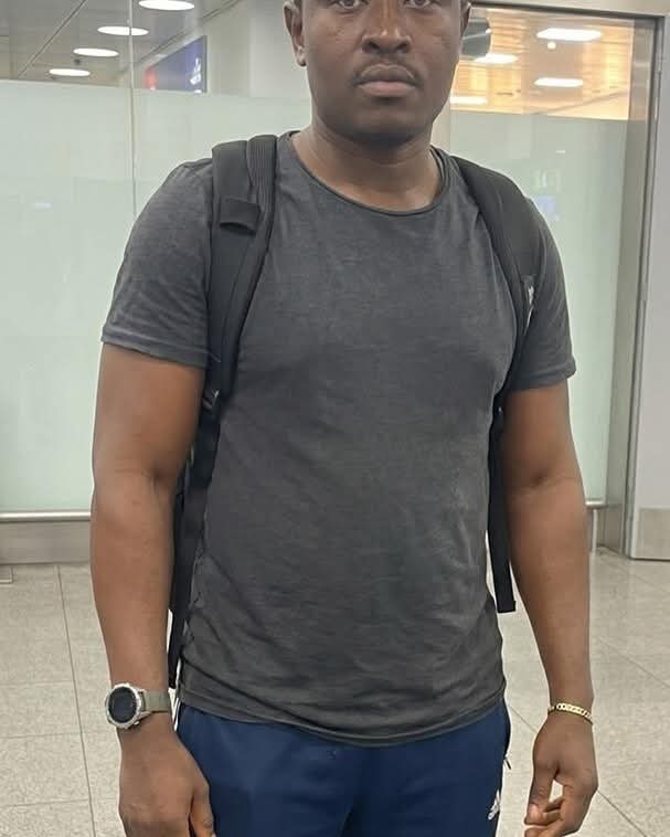 IMG_5721 - THEWILL NEWS MEDIA Man wearing a dark gray T-shirt and black backpack standing in an indoor public space, wearing a smartwatch on his left wrist and a gold bracelet on his right wrist.