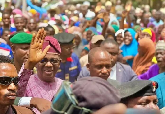 Matawalle Leads Zamfara APC Man in pink traditional attire waves to a crowded outdoor gathering.