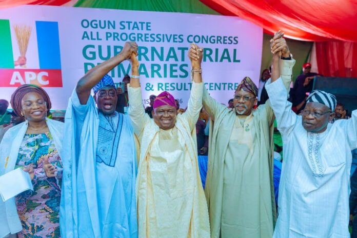 Ogun-APC-governorship-candidate-Senator-Solomon-Olamilekan-Adeola-being-officially-presented-at-the-party-secretariat-after-his-emergence Five people on a stage raise their clasped hands in celebration at a political rally with an APC banner in the background.