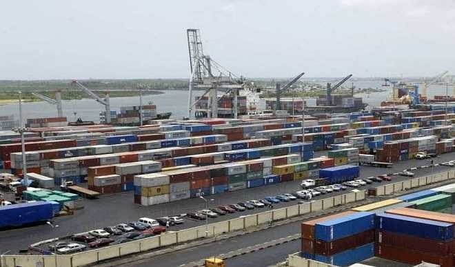 Busy port scene with rows of colorful shipping containers, cranes, and dockside equipment by the water.