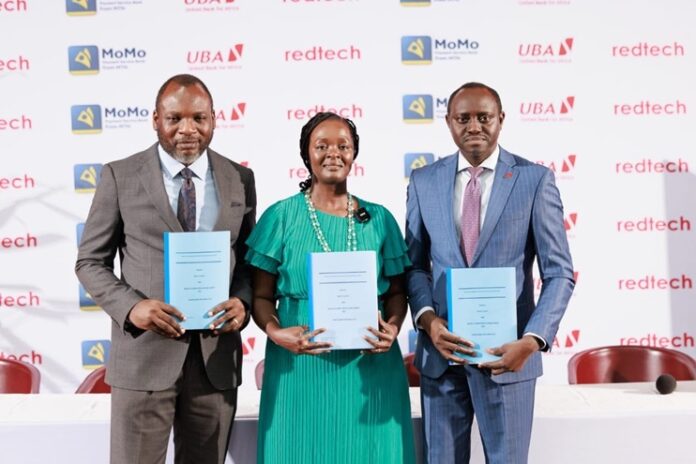 UBA, Redtech, MoMo PSB Expand Merchant Payment Access Across Nigeria Three adults in formal attire stand side by side, each holding a blue folder at a conference with sponsor logos in the background.