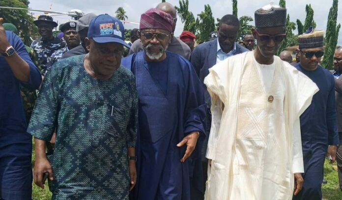 Visit to Oyo Group of men in traditional Nigerian attire walking outdoors, center figures in blue and white gowns with onlookers behind them, greenery in the background