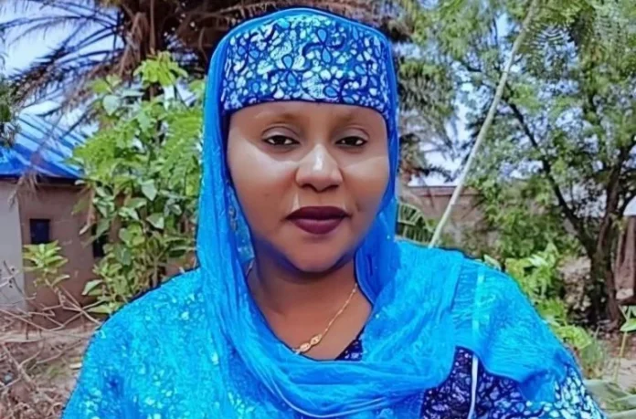 Wasila-Ismail Woman in a bright blue traditional outfit and patterned headscarf outdoors, facing the camera with a neutral expression.