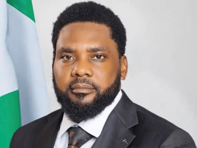 Portrait of a man in a dark suit and tie, with a Nigerian flag in the background.