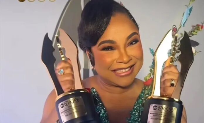 ‘My Father’s Shadow’ Linda Ejiofor Makes History with Double Wins Smiling woman in a sparkly green dress holds two tall award trophies, posing for a celebratory moment at an event.
