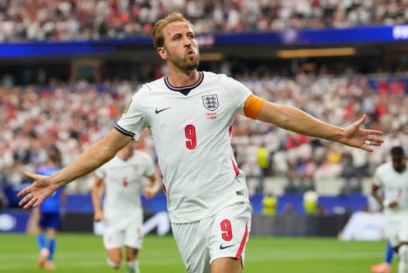 England footballer celebrating a goal in a white jersey with number 9, arms outstretched on a crowded stadium