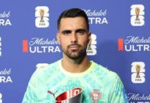 Colombia Top Group K As Portugal Hold Firm In Goalless Miami Stalemate Portugal national team goalkeeper holds a silver trophy in a turquoise jersey at a podium, blue sponsor backdrop behind him