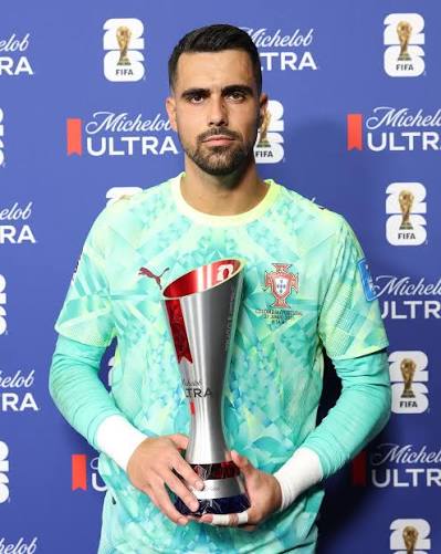 1002324015 Portugal national team goalkeeper holds a silver trophy in a turquoise jersey at a podium, blue sponsor backdrop behind him