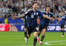 Messi Comes Off Bench As Argentina Finish Perfect Group Campaign With Victory Over Jordan Two soccer players in blue jerseys celebrate a goal, arms outstretched as fans cheer in the stands.