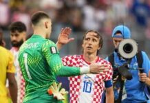 Modrić Inspires Croatia Past Ghana To Set Up Portugal Showdown Croatian footballer in red-and-white checkered jersey (number 10) shakes hands with a green-clad goalkeeper on the pitch as a photographer films in the background.