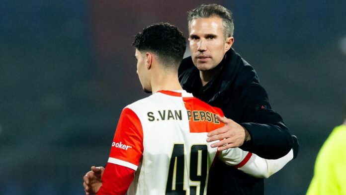 Soccer player S. van Persie wearing a white-red jersey being hugged by a man in a dark jacket on a pitch.