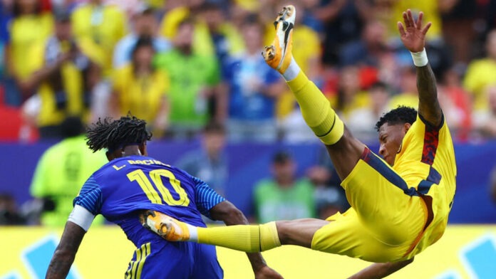 Soccer goalkeeper in yellow dives to block a shot as a blue jersey #10 player challenges nearby.