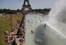 Europe Heatwave Death Toll Exceeds 250 as Temperatures Soar Above 40°C Crowded Paris riverside near the Eiffel Tower, with people sunbathing on the grass and a large water fountain spraying in the foreground.