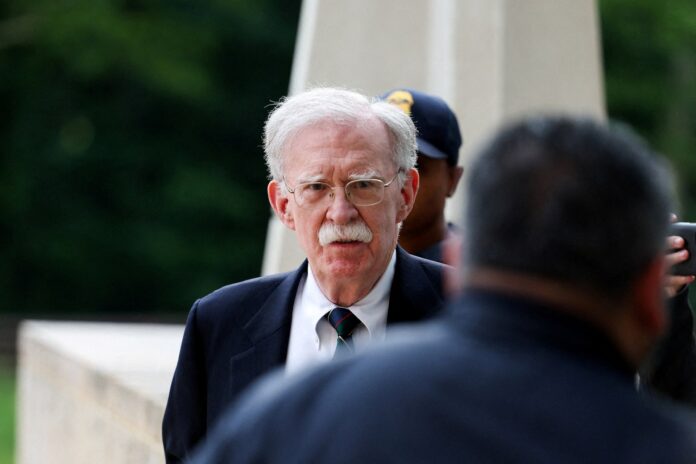 2Q5T2HRM6NPSXG7C6NUL7W5IFI Elderly man with white hair and mustache in a dark suit and striped tie, outdoors with a blurred figure nearby.