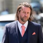 Hollywood Director Carl Rinsch Sentenced To Two And Half Years For $11m Netflix Fraud Man in a navy suit with pink tie and pocket square walking on a city street.