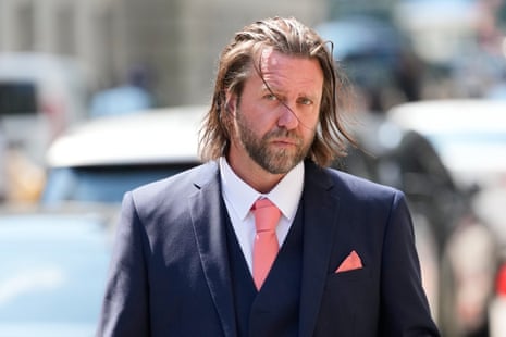 4540 Man in a navy suit with pink tie and pocket square walking on a city street.