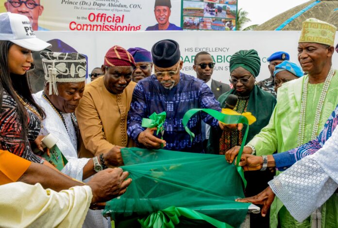 464538 Dignitaries and community members cutting a green ribbon at a formal ceremony.