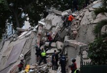 Venezuela Declares State of Emergency After Twin Powerful Earthquakes Rock Capital Rescue workers in hard hats and vests climb amid collapsed concrete and rubble of a building with exposed rebar, at a disaster site.