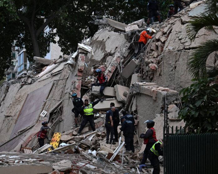 4925 Rescue workers in hard hats and vests climb amid collapsed concrete and rubble of a building with exposed rebar, at a disaster site.