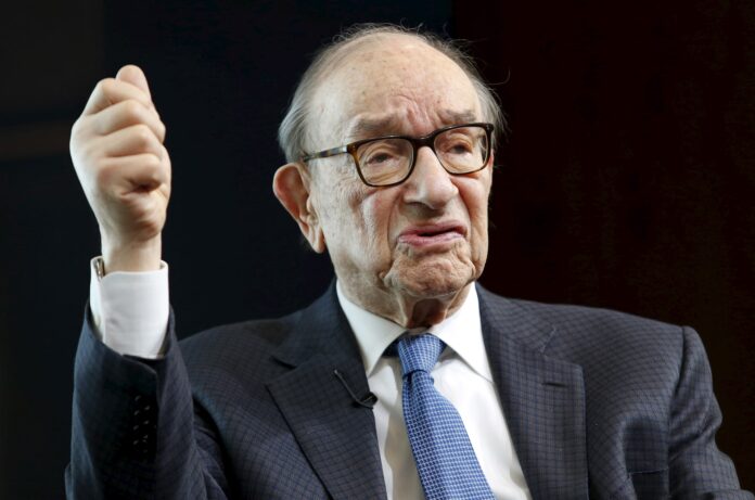 AXZMVFXIJZMEFHZZF5ELZER7AI Older man in a dark checked suit with glasses raises his right fist in a determined gesture against a dark background.