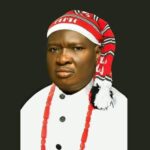 Akwa Ibom: Mboho Mkparawa Ibibio Elects New International President Portrait of a person in ceremonial attire: white robe, red beaded necklace, and red-and-white headwrap against a dark background