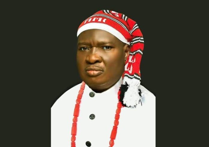 Portrait of a person in ceremonial attire: white robe, red beaded necklace, and red-and-white headwrap against a dark background
