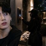 Woman Sentenced To One Year, Faces Deportation For Stalking BTS’ Jungkook Young man in a black jacket gazes off to the side as a nighttime city scene shows a woman at a building intercom and police with a patrol car in the background.