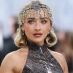 Sabrina Carpenter Granted Five-Year Restraining Order Against Alleged Stalker Portrait of a woman on a red carpet wearing an ornate jeweled headpiece and a metallic halter dress with curled blonde hair.