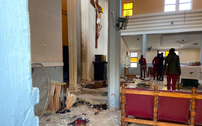 Church-burnt-in-Owo-e1771448986210 Interior of a church with debris scattered on the floor, a crucifix on the wall, and people near the altar assessing the scene