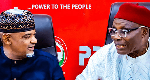 Two Nigerian men in traditional attire smiling before a red campaign banner that reads 'POWER TO THE PEOPLE' with a PDP logo.