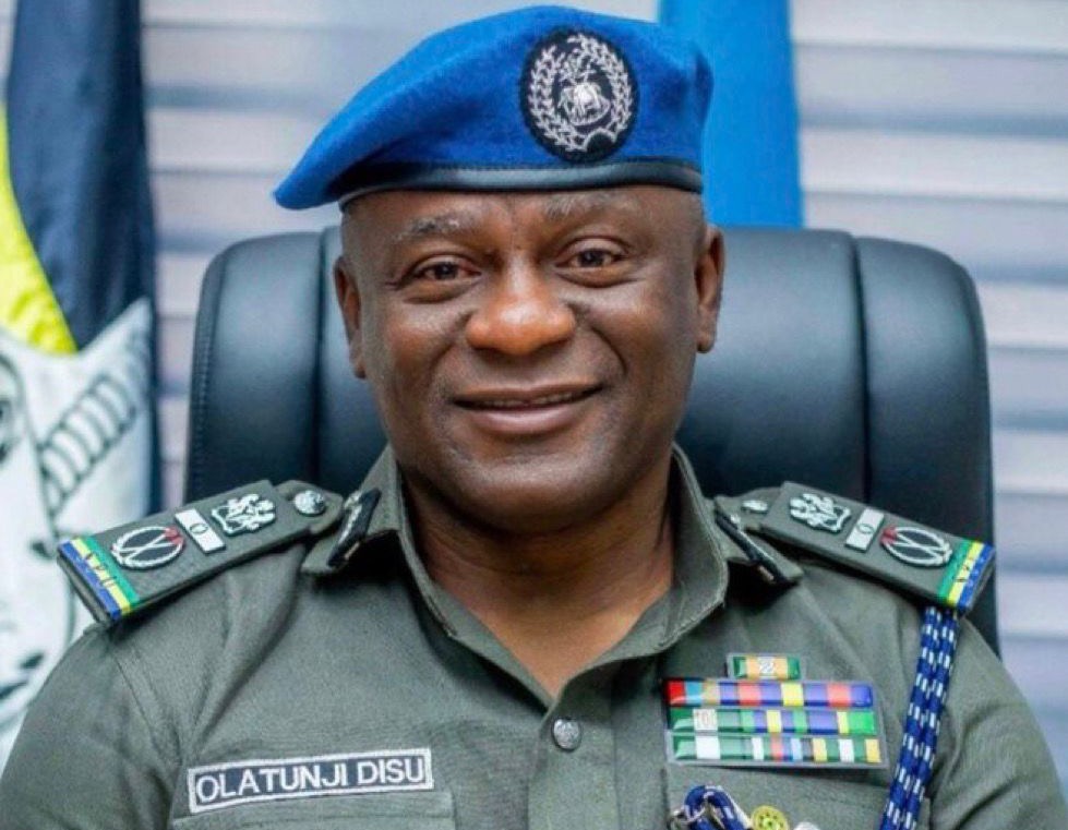 IGP-Tunji-Disu - THEWILL NEWS MEDIA Smiling military officer in green uniform with a blue beret and ribbon bars, seated in an office setting.