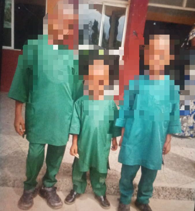 IMG-20260604-WA0007 Three people standing outside a building, wearing matching green outfits: an adult on the left and two children.