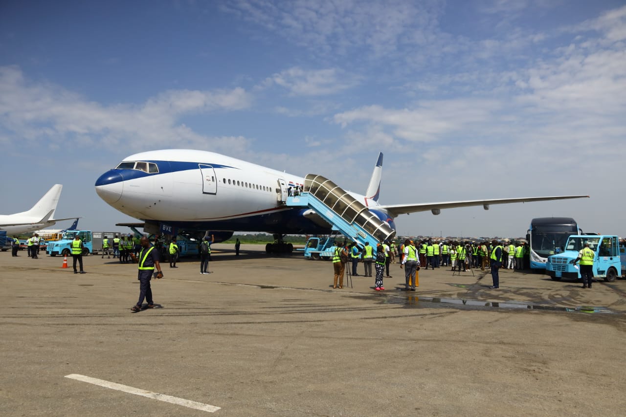 Airplane on tarmac with boarding stairs deployed and ground crew in high-visibility vests nearby.