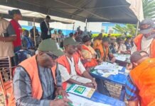 THEWILL EDITORIAL: Malpractices Mar Ekiti Gov Poll Group of people in orange vests seated at blue tables under a tent, filling out forms for an election event.