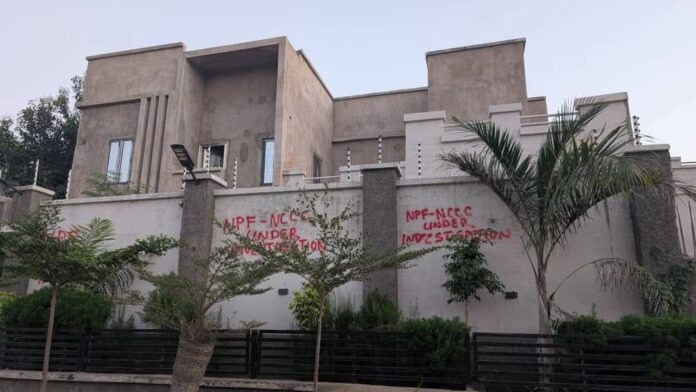 IMG_6092 A modern concrete house with a high wall and a palm tree in front; red graffiti on the wall suggesting something about an investigation.